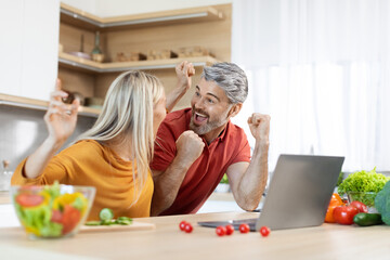 Emotional husband and wife clenching fists in front of laptop