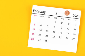A February 2023 calendar and wooden push pin on yellow background.