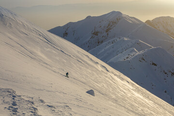 A freerider snowboarder descends a wide slope against the background of mountain ranges and the sunset
