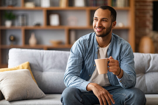 Portrait of handsome african american man resting on couch with cup of coffee