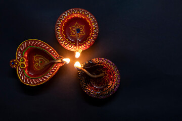 Happy Diwali. Three clay dia lamps are burning on a black background. Deepa festival of Hindus. Can be used for advertising banner, poster background