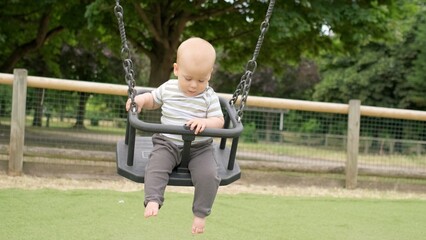 Funny Little Younger Newborn Infant Brother Boy On Swing. Baby Playing On Playground. Summer time outside. Kids Entertainment, Childhood, Child Development, Happy Family Concept