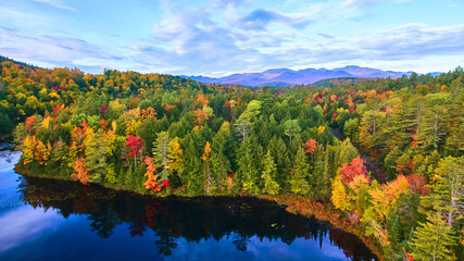 Aerial over blue lake with fall forest hills around and mountains in distance