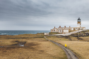 Fototapeta na wymiar A person in a yellow jacket walking the road leading to the lighthouse Neist Point, Scotland