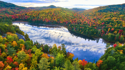 Morning light shines over reflective lake and stunning mountains of peak fall foliage