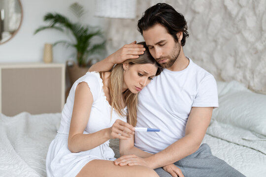 Infertility problem. Caucasian couple sitting on bed with negative pregnancy test result