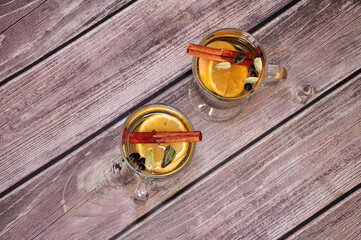 Two glasses of herbal tea with lemon, cinnamon and spices on a wooden table.
