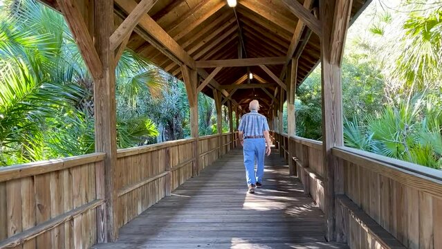 Elderly man walking down covered bridge in a botanical garden