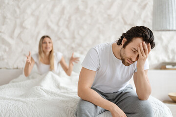 Angry woman shouting at her husband, having conflict while sitting on bed at home, focus on upset...