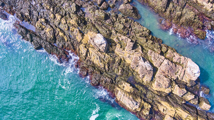Aerial down of rocky coast section with crashing waves