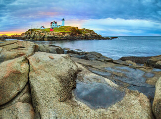 Boulders and puddles of Maine coast looking at stunning Maine lighthouse during dawn morning light