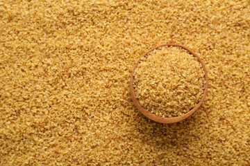 Wooden bowl on pile of uncooked bulgur, top view. Space for text