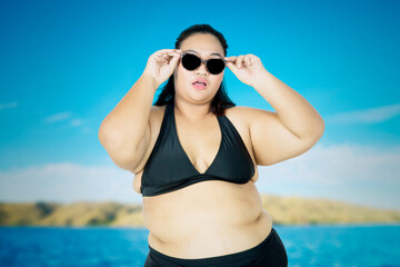Obese woman wear sunglasses and bikini on beach