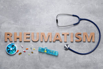 Word Rheumatism made of wooden letters, stethoscope and pills on light gray textured background,...