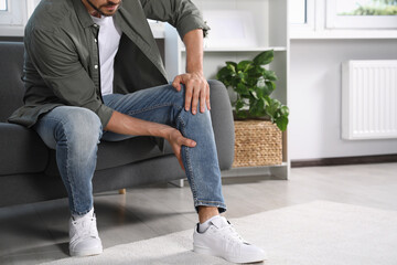 Man suffering from pain in leg on sofa at home, closeup. Space for text