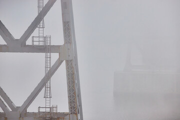 Support pillars of old steel bridge with ladders fading in extreme weather foggy morning