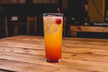 Colorida bebida de tequila con jugo de naranja, sangría y cereza, sobre una mesa de madera