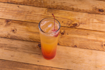 Colorida bebida de tequila con jugo de naranja, sangría y cereza, sobre una mesa de madera