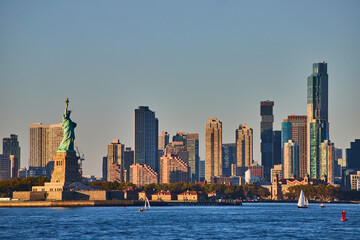 Statue of Liberty with skyscrapers surrounding from waters in golden light