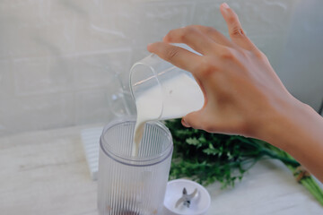 Close-up of a woman pouring milk into a small portable blender to make a smoothie