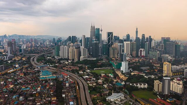 Aerial high angle sunset view time lapse overlooking busy expressway and streets against a city skyline and an urban village at dusk in Kuala Lumpur, Malaysia. Prores 4KUHD Timelapse.