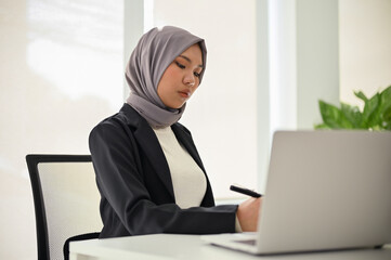 Professional Asian Muslim businesswoman concentrating on her business tasks, working in office