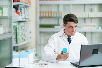 Male pharmacist working in modern pharmacy using laptop.