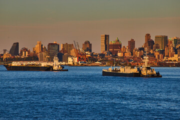 Obraz premium Pair of industrial merchant ships in New York City bay in golden hour with city behind