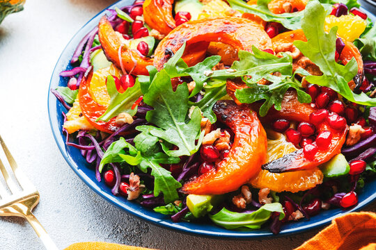 Fresh pumpkin salad with red cabbage, avocado, lettuce, arugula, pomegranate and nuts. Vegan healthy eating, slow comfort food. White table background. Top view