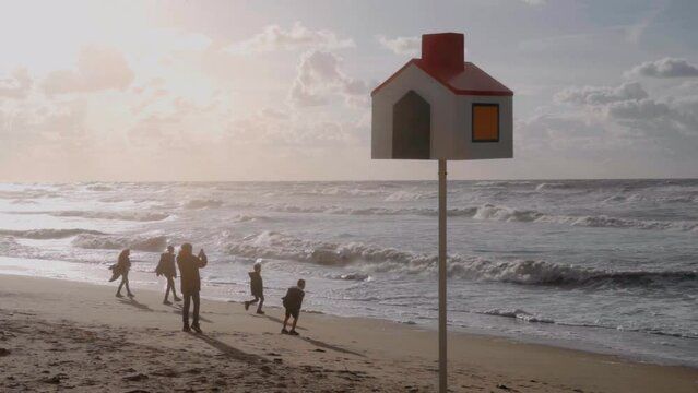 Silhouette of happy family playing with the wind on the beach with an orientation pole in the foreground - De Haan, Belgium