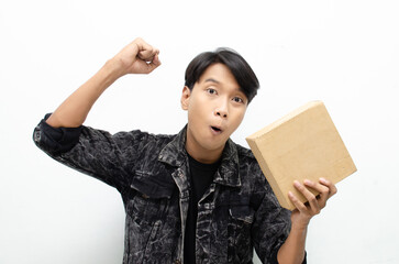 Young Asian man holding package over white background, smiling and excited. Concept of delivery courier and shipping services