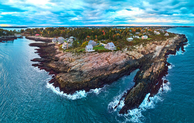 Stunning aerial over rocky coasts of Maine on the ocean with houses, fall foliage, and dusk light