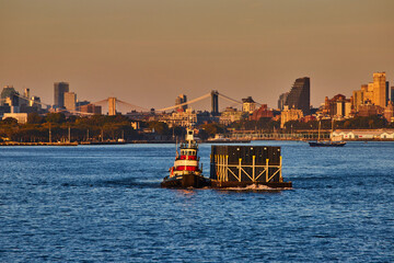 Small industrial ship pulling shipping containers from side in industrial New York City golden hour