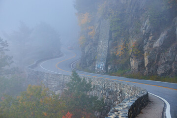Foggy road with stone wall winding along cliffs into foggy morning