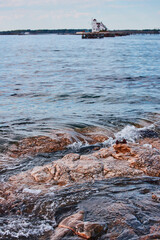 Naklejka premium Detail of small waves crashing on rocks in Maine with house on island in background