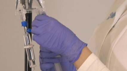 Nurse holding syringe and adding fluid to the saline bag of IV stand for intravenous therapy