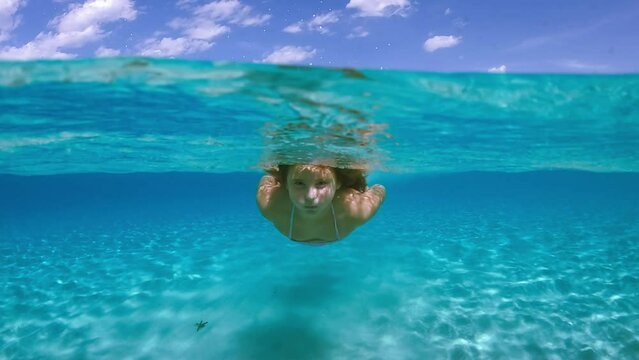 Child girl swims toward camera beneath sea water surface of Saleccia exotic beach in Corsica island, France. Waterline slow motion view