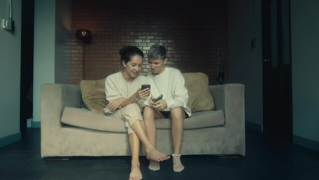 Two young women sitting with their phones on the couch in their home