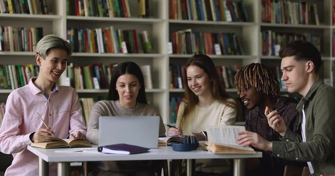 Five diverse students sit at table studying together staring at laptop screen, discuss task looking friendly and positive. Gen Z people learn, gain new knowledge, improve skill, get higher education