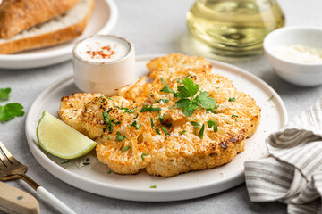 Cauliflower steaks with sauce on white plate, vegetarian dish, selective focus