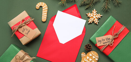 Envelope with blank Christmas greeting card, gift boxes, cookies and decor on green background, top view