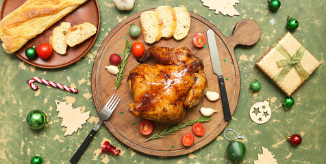Board with tasty roasted chicken, bread, Christmas gift and decor on green background