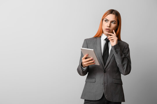 Thoughtful transgender secretary with tablet computer on grey background
