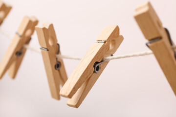 Wooden clothespins hanging on rope against color background, closeup