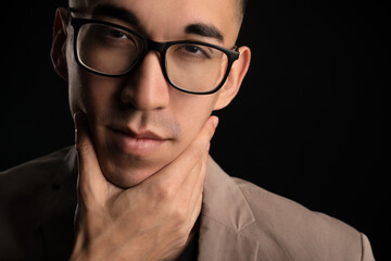 Fototapeta na wymiar Young Asian man in eyeglasses touching face on black background