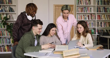 Positive multi ethnic students studying together using laptop in library, high school teenagers talking, discuss collaborative task during meeting. Generation Z and modern wireless technology usage - Powered by Adobe
