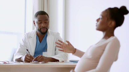 Pregnancy checkup. Young pregnant black woman sitting at doctor's appointment, professional therapist taking notes