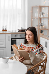 Young woman reading book at dining table in kitchen