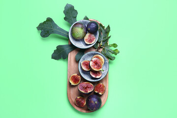 Wooden board with bowls of fresh figs and leaves on green background