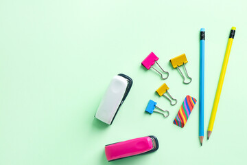 Staplers, paper clips, eraser and pencils on color background